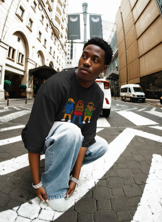 Person wearing a black t-shirt with colorful graphics and light blue jeans, crouching on a city street.
