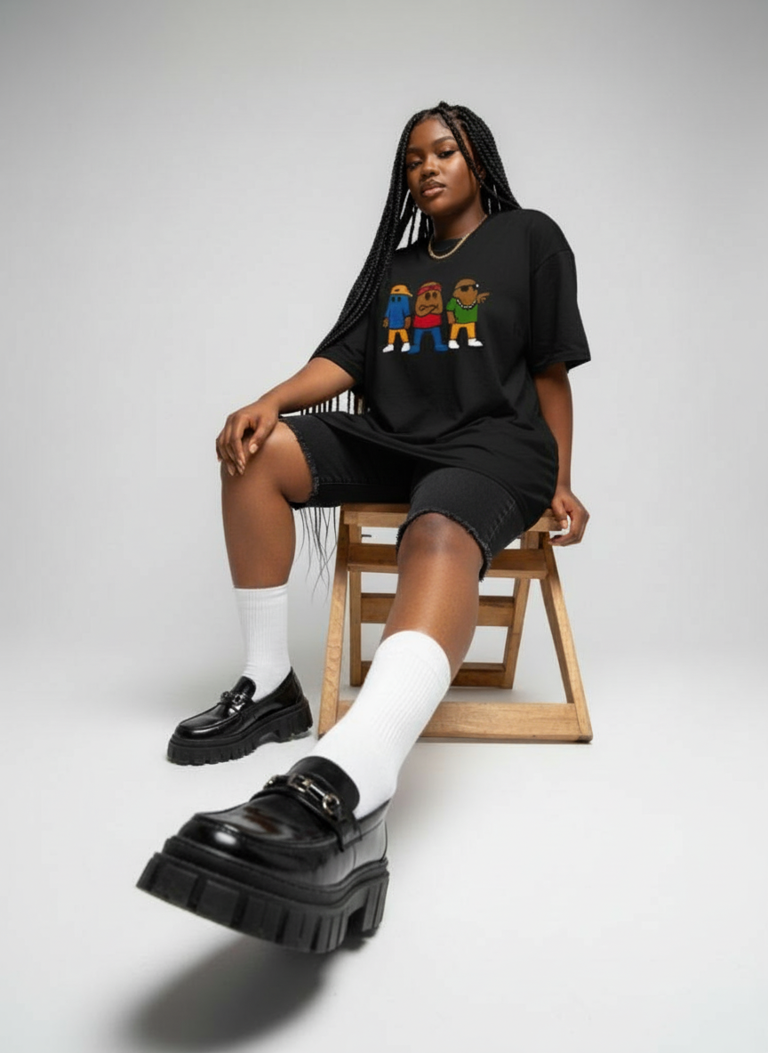 Person wearing a black oversized t-shirt with colorful graphics, black shorts, white socks, and black platform shoes on a light gray background.