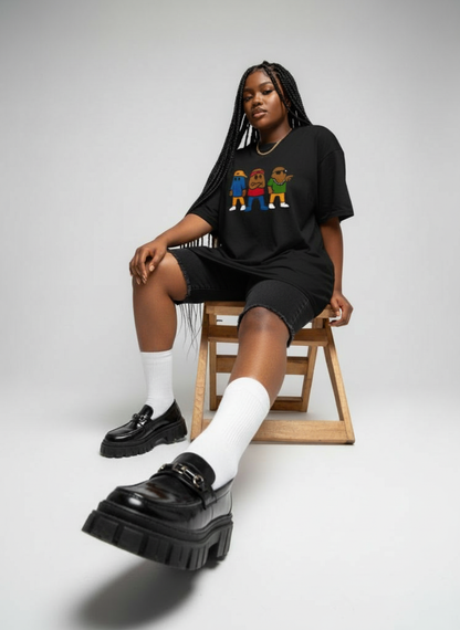 Person wearing a black oversized t-shirt with colorful graphics, black shorts, white socks, and black platform shoes on a light gray background.